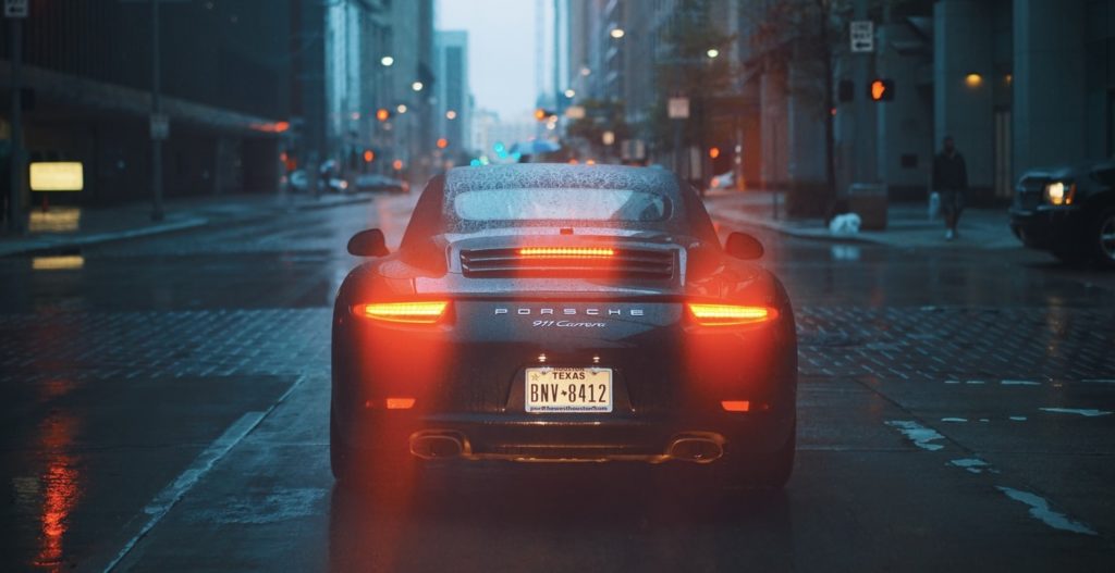 Porsche driving away on rain shiny streets at night